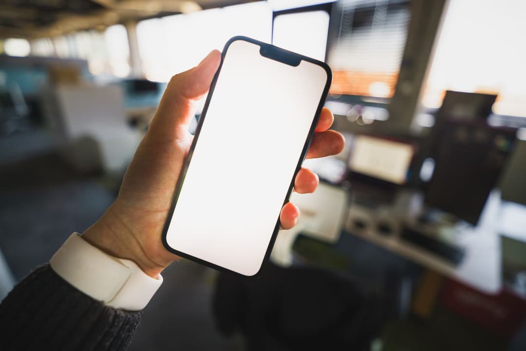 A hand holding a smartphone in a bright office