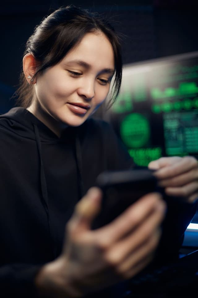A developer looking at a phone in front of screens of code