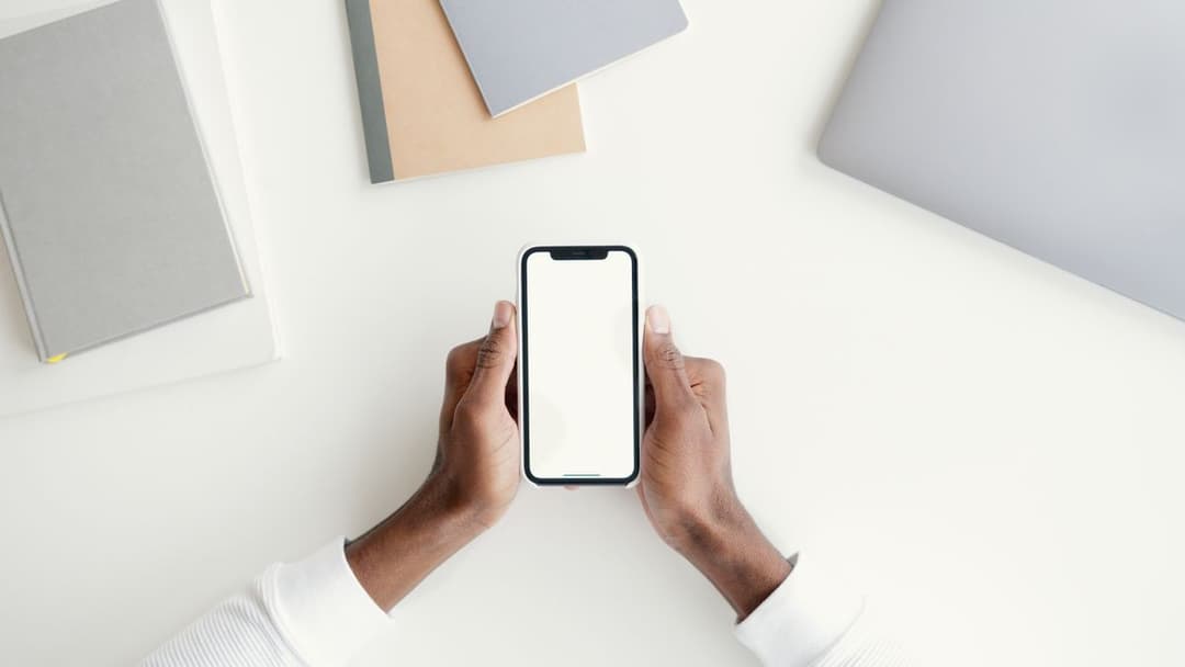 Hands holding a smartphone with a blank screen over a desk
