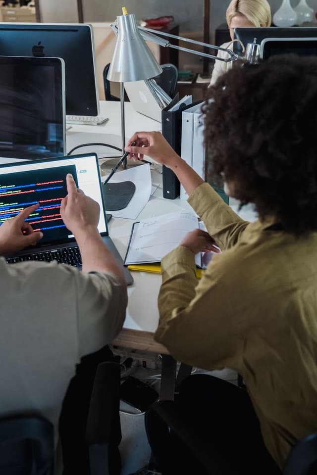 Two people pointing at code on a laptop during a review