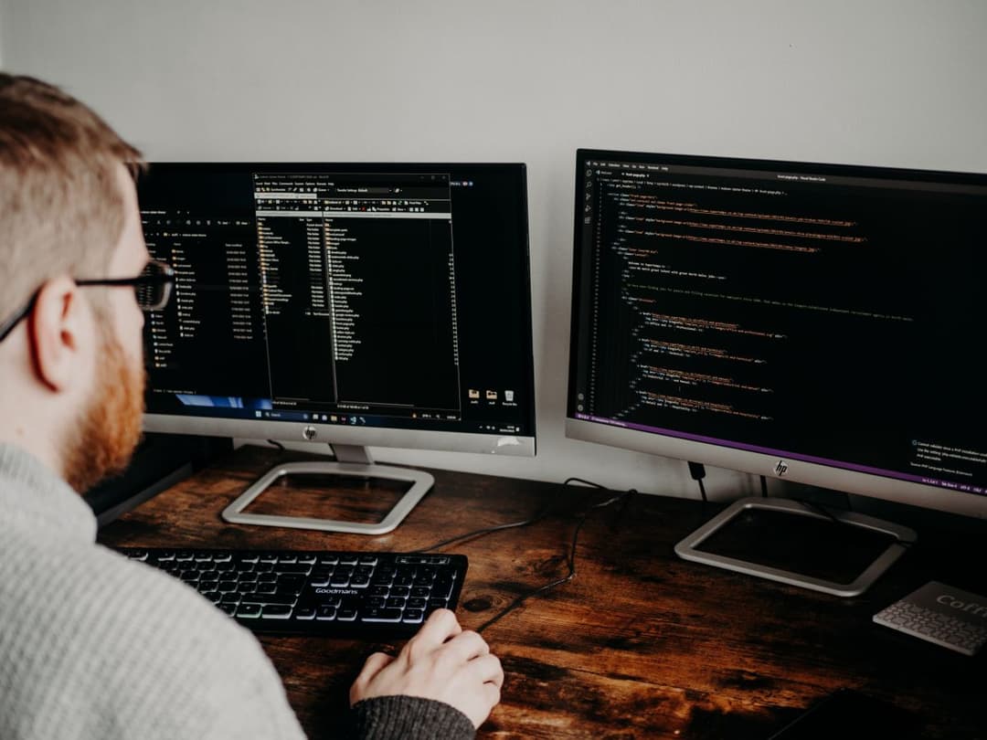 A developer working on code across two monitors
