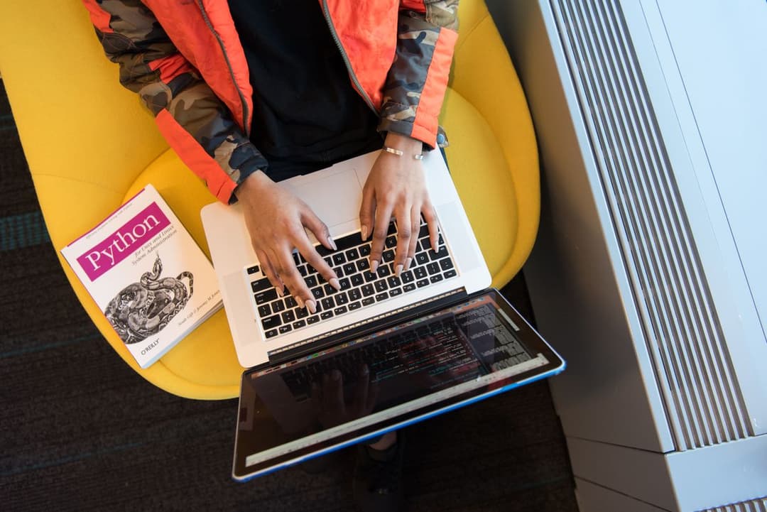 A developer coding on a laptop with a programming book nearby