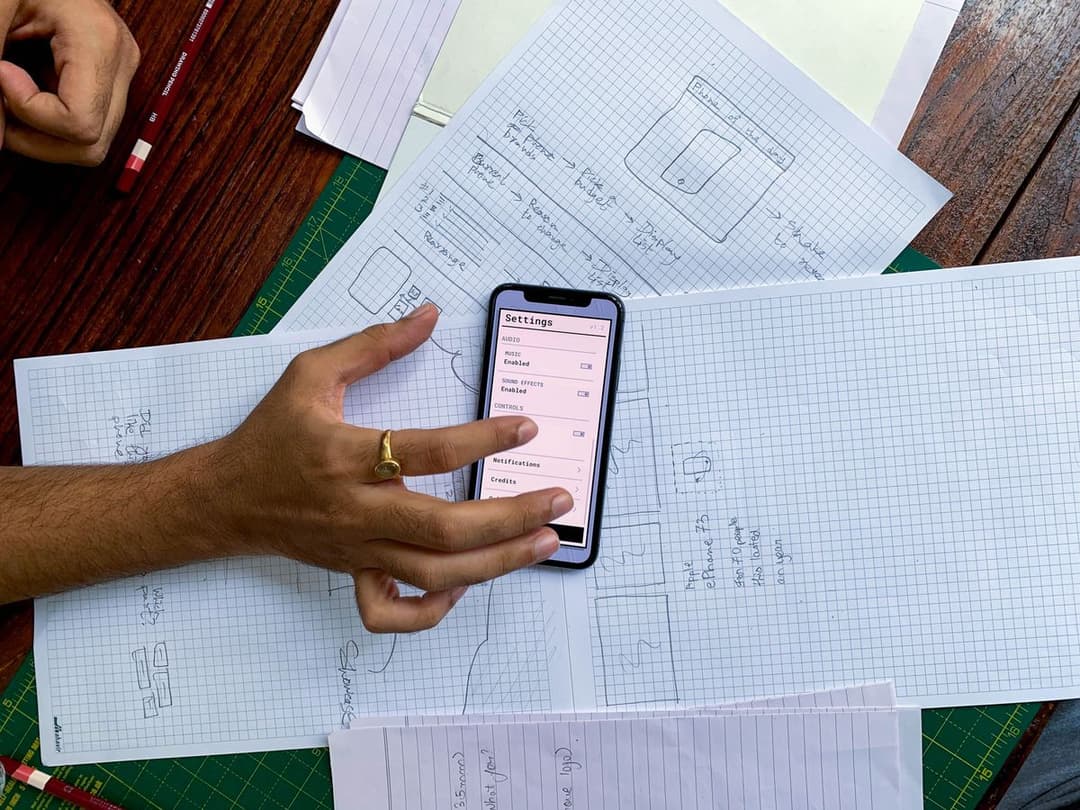 A hand holding a smartphone above app wireframe sketches