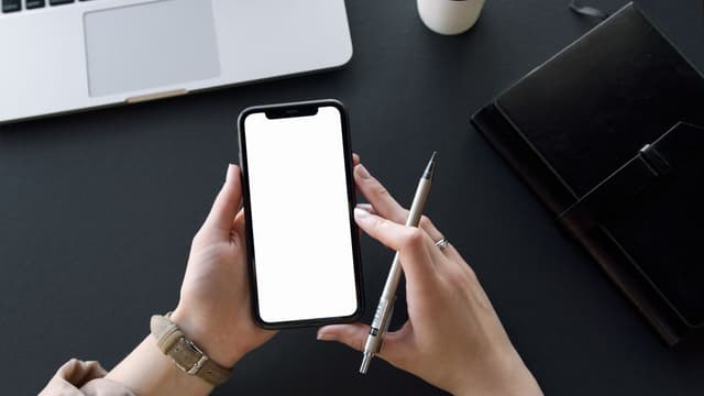 Hands holding a smartphone with a blank screen at a desk