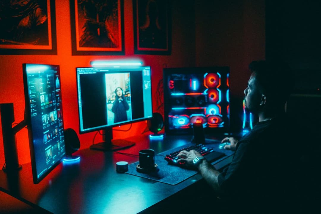 A developer working at a multi-monitor setup in a neon-lit room